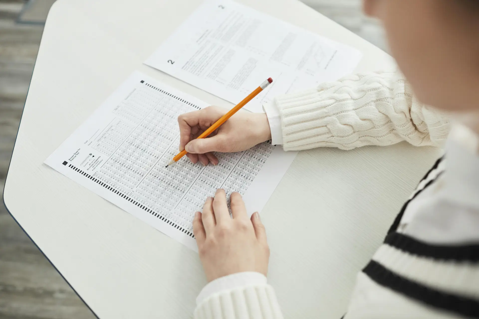 Close-up of a student filling out a multiple-choice exam in a quiet classroom setting.