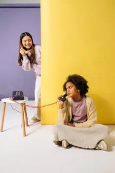 Two girls having fun using a colorful retro phone in a playful setting.