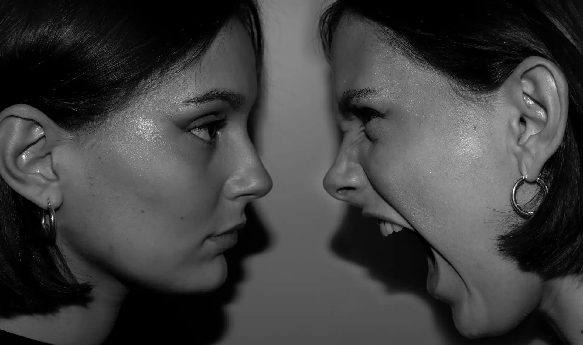 Intense black and white close-up of two women expressing contrasting emotions facing each other.